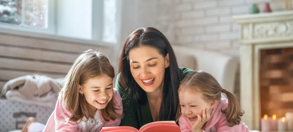 Mom and two daughters laying on the floor reading a book