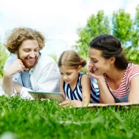 Family of three laying on the grass outside looking at a tablet