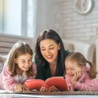 Mom and two daughters laying on the floor reading a book