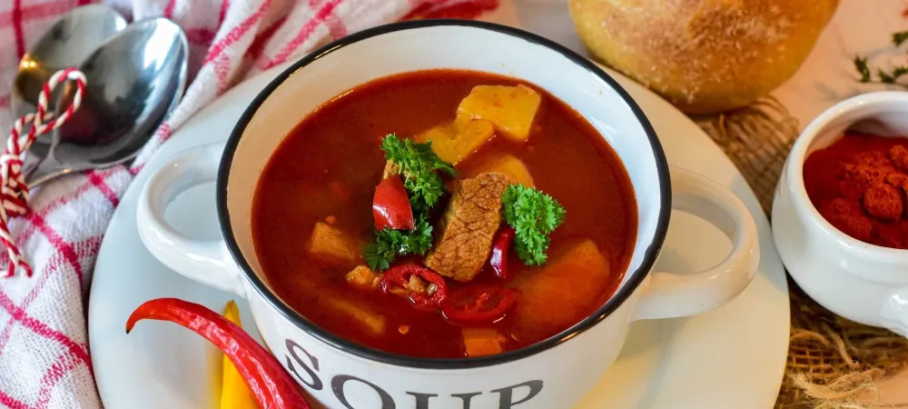 Soup in a bowl that is on a plate with bread and peppers next to it