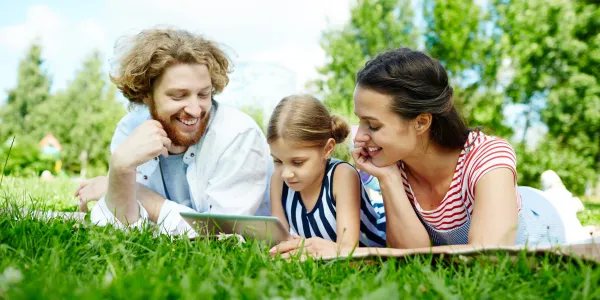 Family of three laying on the grass outside looking at a tablet
